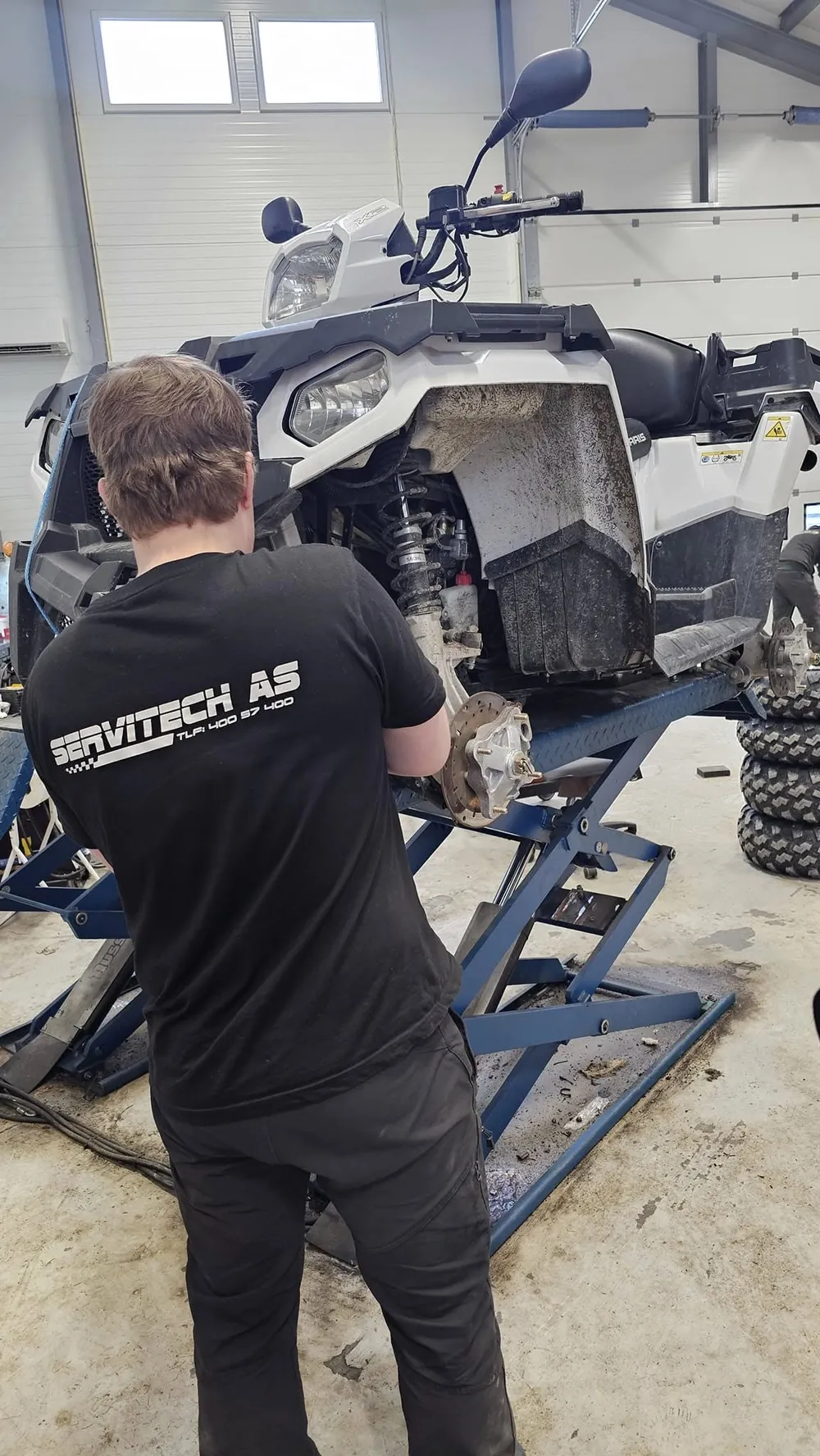 Mekaniker i Servitech-genser reparerer en Polaris ATV på løftebord