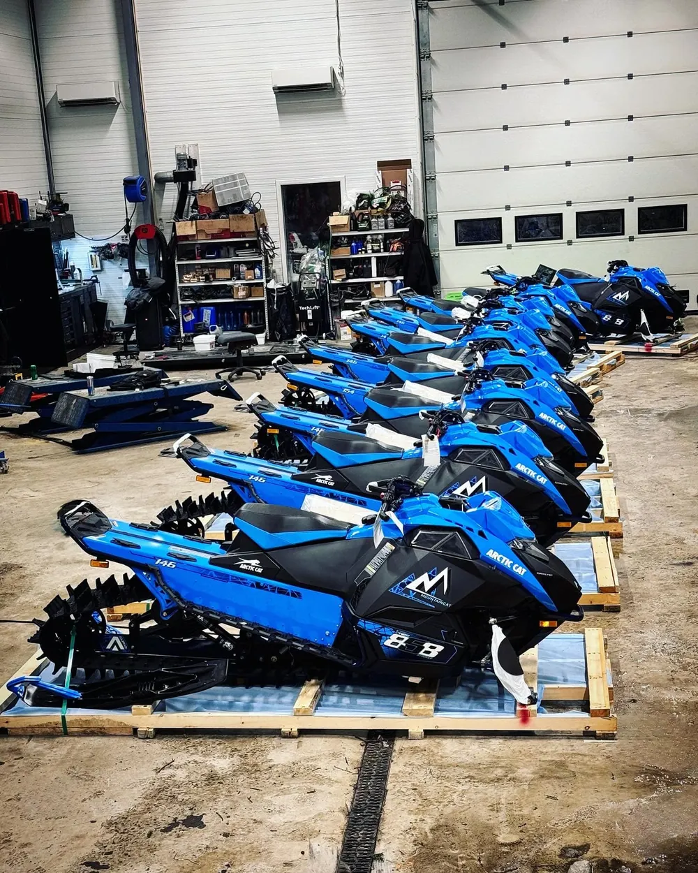 Rad med nye blå Arctic Cat Mountain Cat-snøscootere klare til levering i verkstedet